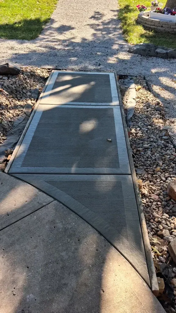 Scored concrete walkway with decorative rock border and landscaping
