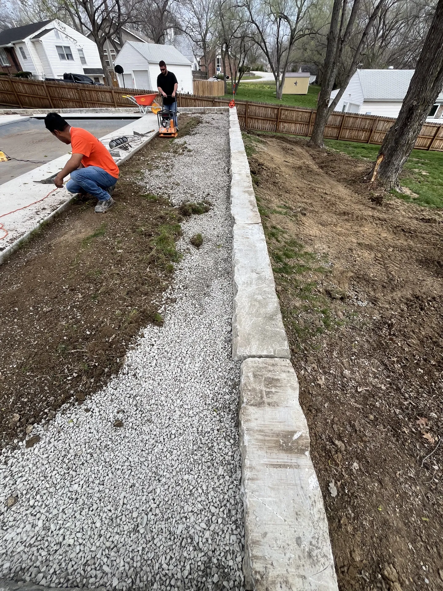 Long retaining wall curb with gravel and worker